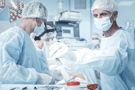 I need this. Responsible confident skilled medic standing in the operational working and taking the instrument.の写真素材