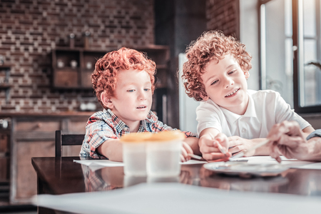 Creative outlet. Joyful cute nice boys sitting at the table and looking at the painting process while enjoying itの写真素材