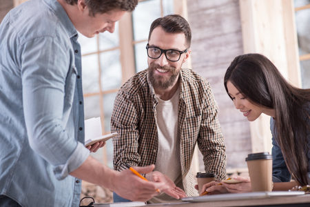 Students cooperation. Happy nice smart students standing together and working in team while preparing a projectの写真素材