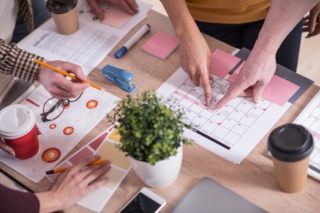 Important date. Delighted nice positive people standing together and pointing at the calendar while choosing a dateの写真素材