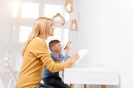 Modern technology. Delighted happy nice mother and son sitting together and looking at the virtual screen while using modern technologyの写真素材