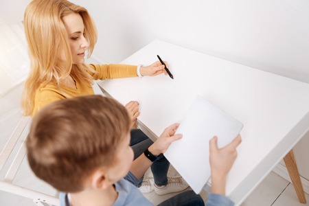 Family relationships. Joyful nice positive mother and son sitting at the table and using virtual technologies while spending time togetherの写真素材