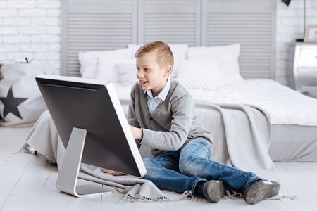 Pleasant entertainment. Delighted happy positive child smiling and sitting in front of the screen...