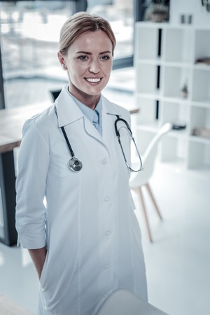 Ready for new task. Skilled pretty confident nurse looking straight and smiling being in the cabinet.の写真素材