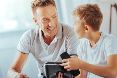 Futuristic technology. Smart positive curious looking at his father and talking to his while discussing new technologiesの写真素材