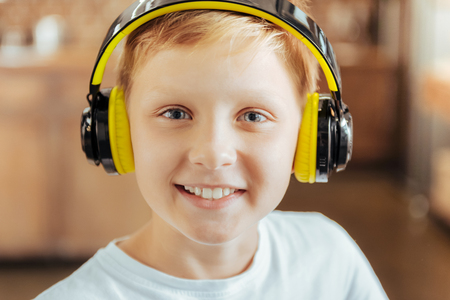 Favourite hobby. Portrait of a positive cute delighted boy smiling and looking at you while wearing headphonesの写真素材