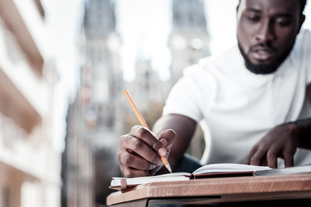 Not to forget. Selective focus on a hand of a millennial guy looking at his notebook while sitting outdoors and taking some notes.の写真素材