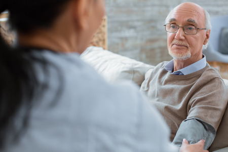 Systolic pressure. Doctor using tonometer and helping pensive calm senior man while checking his blood pressureの写真素材