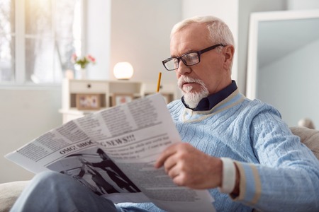 Informative article. Charming elderly man in eyeglasses reading an article in the newspaper and marking interesting passages with the pencilの写真素材