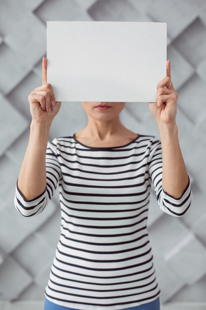 Not to violence. Sad depressed young woman standing against the wall and holding a sheet of paper while showing it to youの写真素材
