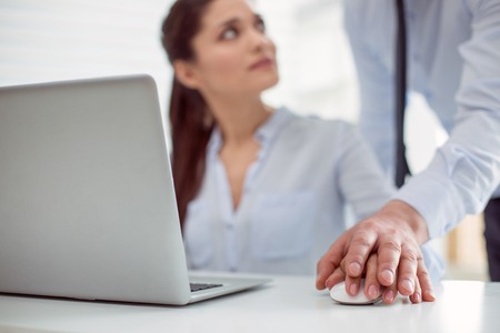 Sexual abuse. Nice pleasant young woman sitting at the table and working while feeling a male hand on hersの写真素材