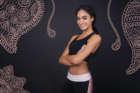 Feeling glad. Cheerful young beautiful sportswoman looking happy and smiling while standing alone with her arms crossedの写真素材