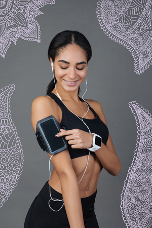 Switch on. Emotional young professional trainer smiling and touching a modern smartphone while switching on the music before doing exercisesの写真素材