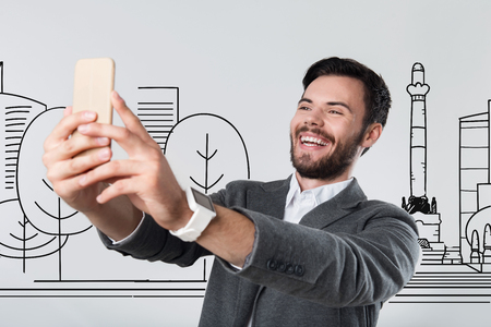 Taking photos. Emotional active cheerful tourist feeling happy while travelling and taking photos of himself in a beautiful cityの写真素材