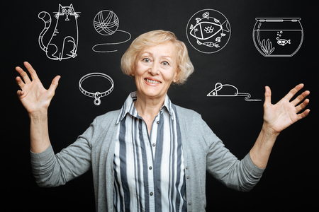 Pets lover. Cheerful kind senior lady smiling and putting her hands up while being alone and thinking about her cute adorable petsの写真素材