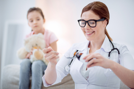 Necessary medication. Cheerful merry female doctor pouring medication for helping girl while posing on blurred backgroundの写真素材