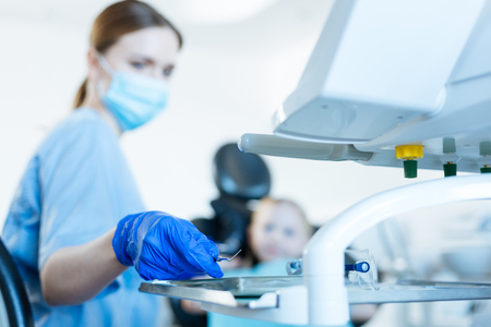 Professional instrument. The focus being on the hand of a pretty young female dentist taking dental probe from tray while conducting an examination of a little girlの写真素材