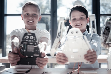 The work is done. Selective focus on positive minded youngster looking into the camera with cheerful smiles on their faces while holding their newly constructed robots.の写真素材