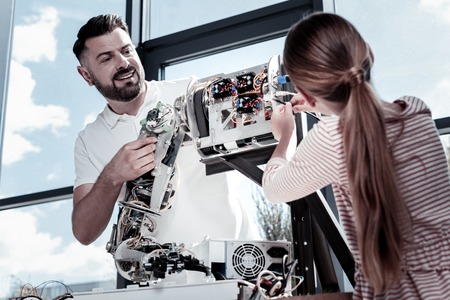 Be careful darling. Low angle shot of a satisfied mature gentleman smiling cheerfully while looking at his student helping him with a robotic machine.の写真素材