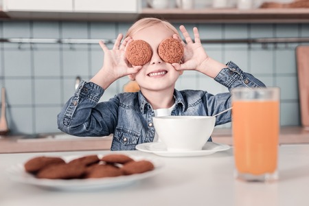 Want to play. Little female keeping smile on her face and raising hands while sitting in the kitchenの写真素材