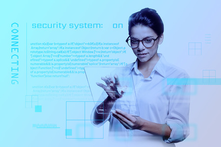 Security system. Beautiful young experienced programmer holding a modern transparent tablet and having her face scanned while working with the newest security systemの写真素材