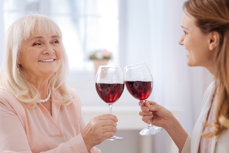 Delicious drink. Close up of glasses with wine being clinked by nice joyful cheerful womenの写真素材