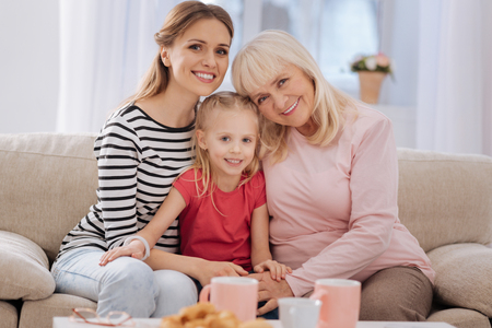 Female generations. Nice happy joyful family sitting together and looking at you while being at homeの写真素材