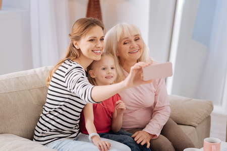 Family photo. Pleasant nice young woman sitting together with her family and smiling while taking a photoの写真素材