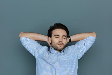 Pleasant nice handsome man closing his eyes and resting while putting hands under his headの写真素材