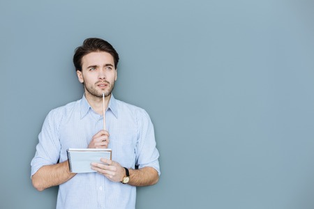 Nice handsome thoughtful man holding a pencil and putting it to his chin while searching for new ideasの写真素材