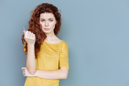 Beautiful woman. Pleasant nice red haired woman standing against grey background and looking at you while holding a cardの写真素材