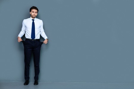 Nice positive bearded man looking at you and showing his pockets while having no moneyの写真素材