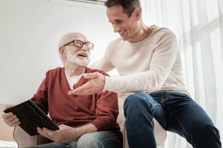 Senior unshaken bespectacled man spending time with a son smiling and holding the tablet.の写真素材