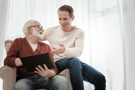 Happy joyful friendly men spending time together sitting on the chair and using the laptop.の写真素材