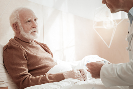 Pleasant interested aged man sitting on the bed looking at a doctor and listening.の写真素材