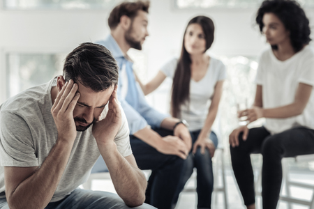 Nice serious upset man sitting on the chair and holding his head while being stressed outの写真素材