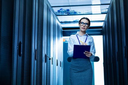 Inspired serious woman taking notes and standing new server cabinetsの写真素材