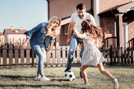 Play together. Friendly lovely happy family having fun laughing and playing football together on the yard.の写真素材