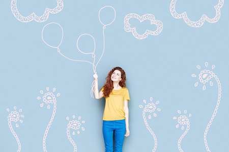 Holding balloons. Cheerful student holding beautiful balloons and feeling happy while going to a birthday partyの写真素材