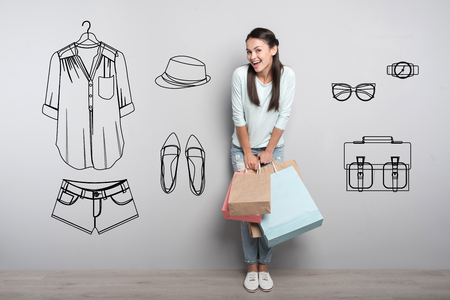 Pleasant shopping. Cheerful emotional young girl feeling happy while standing with paper bags after going shoppingの写真素材