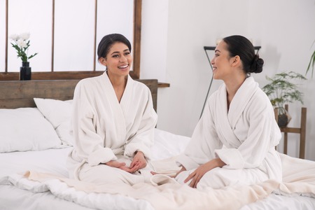 Happy couple. Joyful delighted women sitting in the bed in the spa salon and smilingの写真素材