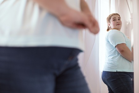 Good figure. Good looking plump woman evaluating her figure while spinning around the mirrorの写真素材