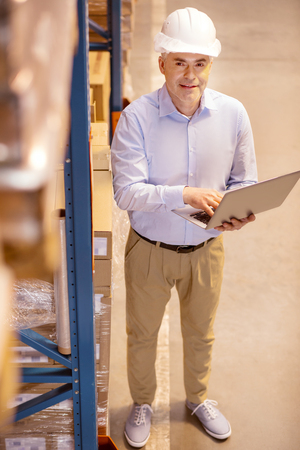 Modern device. Happy smart businessman pressing a button on his laptop while controlling the work of his employeesの写真素材