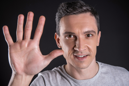 Positive emotions. Portrait of a happy positive pleasant man smiling and showing his palm while standing against black backgroundの写真素材