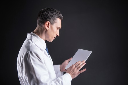 Professional scientist. Serious nice handsome man holding a tablet and doing a professional research while working in the laboratoryの写真素材