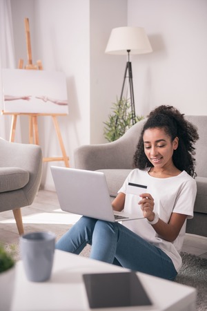 Online money transaction. Nice beautiful woman looking at her credit card while doing an online money transactionの写真素材