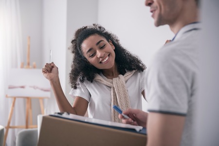 Where to sign. Cheerful happy woman holding a pen while asking the delivery man where to signの写真素材