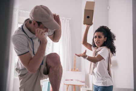 Dissatisfied customer. Angry young woman shouting at the courier while holding a boxの写真素材
