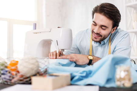 I feel alert. Content dark-haired tailor smiling and working on a sewing machineの写真素材