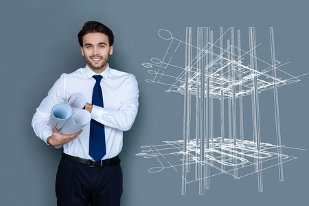 Cheerful architect. Creative experienced architect feeling confident and smiling while holding graphicsの写真素材